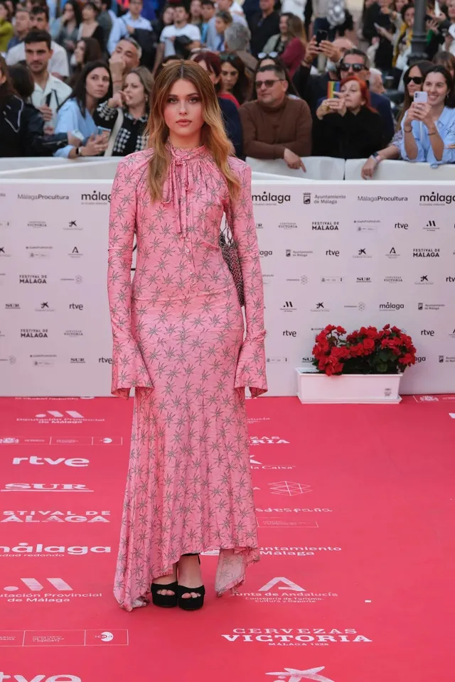 Nicole Wallace posing in a pink floral dress and black platform heels at a film festival.
