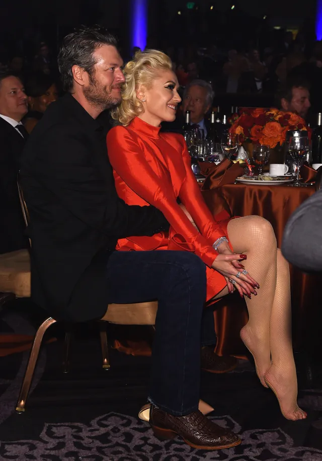 Gwen Stefani sitting beside another person in a red outfit and pointed heels.