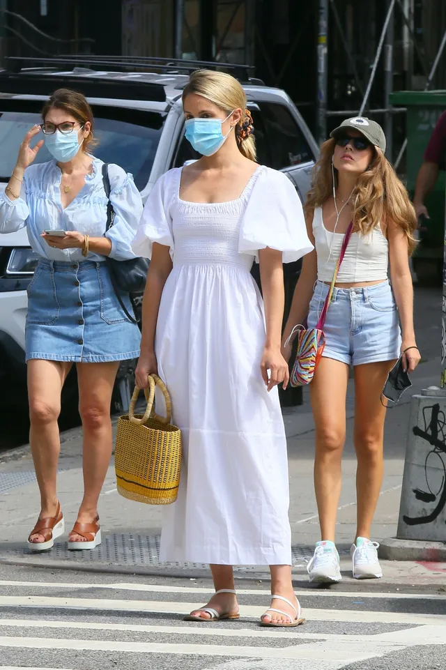 Dianna Agron walking with companions in a white dress and flat sandals.