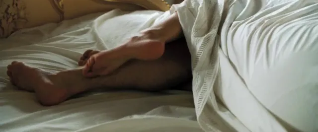Eva Green lying beneath white sheets with bare feet visible.