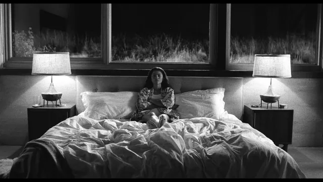 Zendaya: seated barefoot on a bed in a black-and-white portrait.