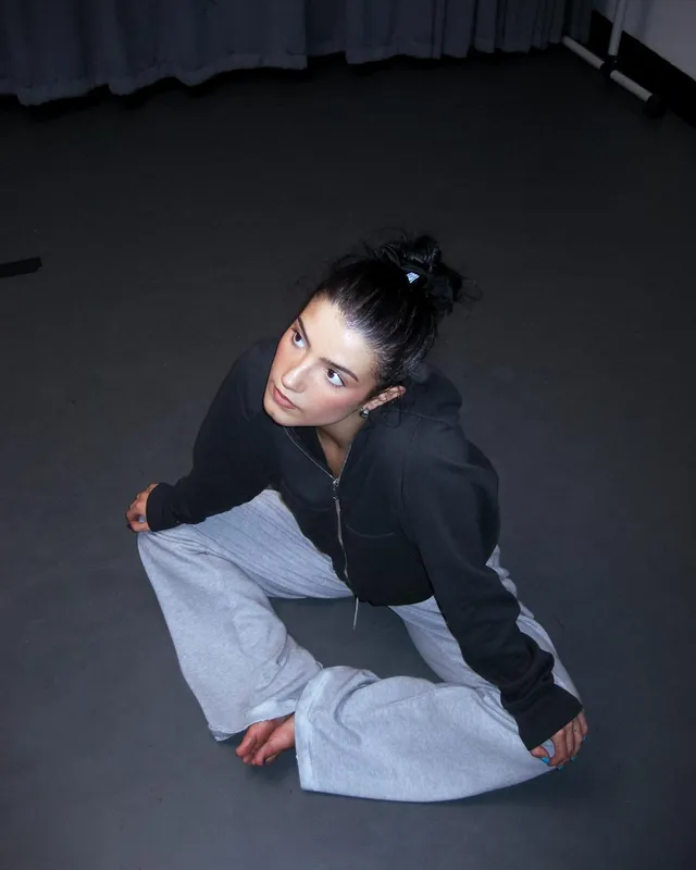 Charli D’Amelio sitting barefoot on a dance studio floor.