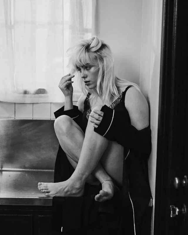 Billie Eilish a monochrome portrait seated beside a window.