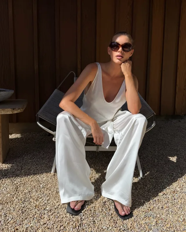 Elsa Hosk sitting in a chair wearing a white outfit and black heeled sandals.
