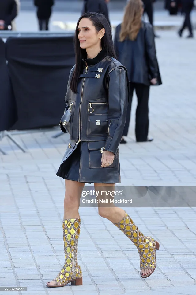 Jennifer Connelly standing outdoors in a denim outfit and patterned boots.