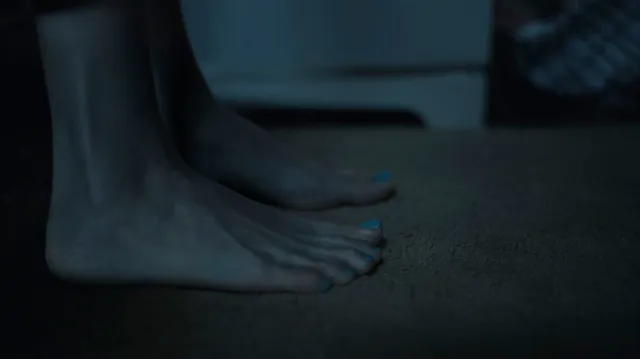Peyton List standing barefoot in a dimly lit screen scene.