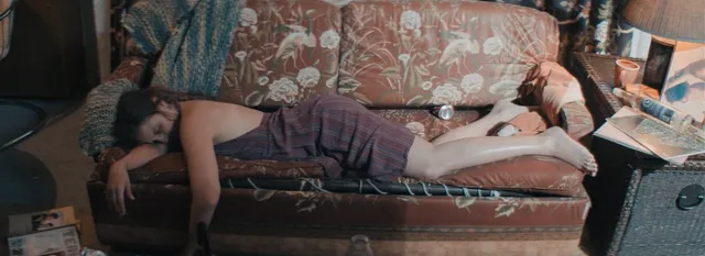 Dianna Agron reclining on a patterned sofa during a screen scene.