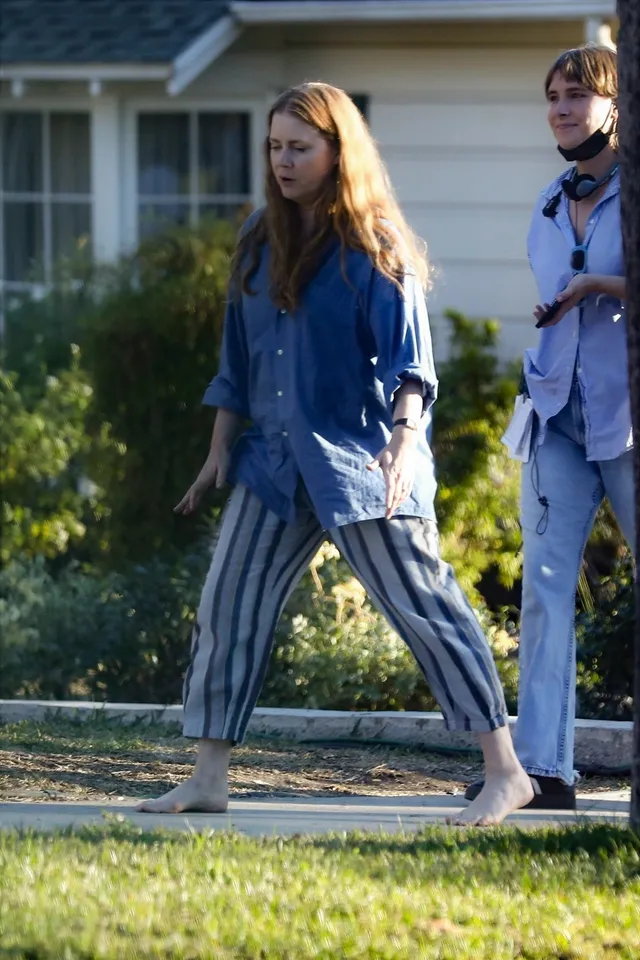Amy Adams walking outside in striped trousers.