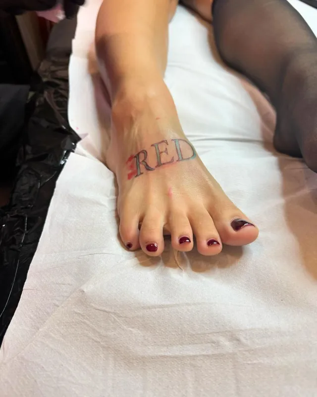 Doja Cat showing a bare foot with dark nail polish and red lettering.