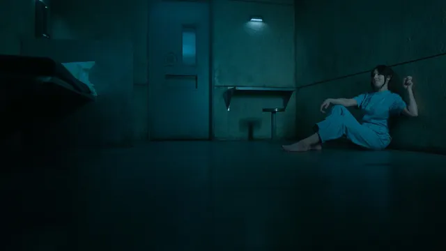 Elizabeth Gillies reclining indoors during a blue-lit screen scene.