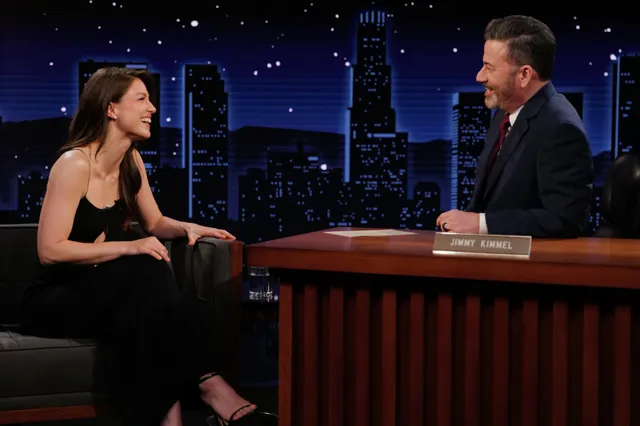 Melissa Benoist sitting in a dark dress and heels for a television interview.