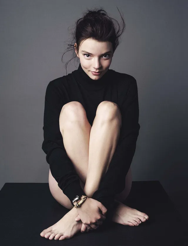 Anya Taylor-Joy sitting barefoot in a black studio outfit.