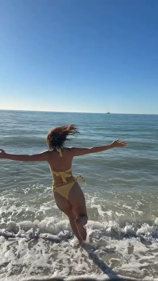 Millie Bobby Brown walking into the sea in a yellow swimsuit.