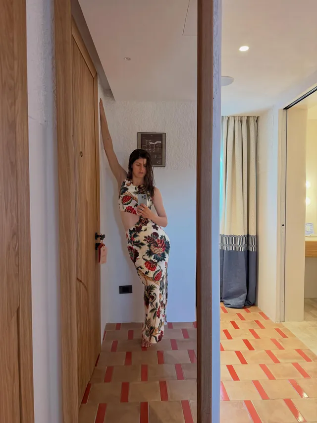 Alexandra Daddario taking a barefoot mirror photo in a floral dress.