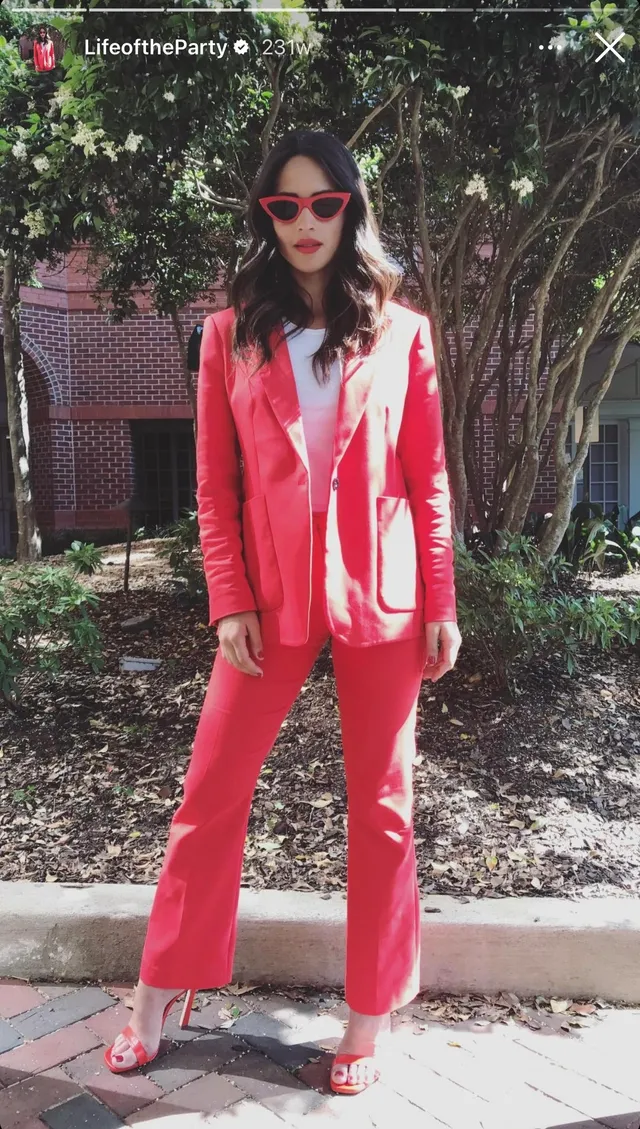 Adria Arjona wearing a coral suit and pale heeled sandals outdoors.