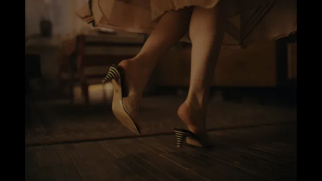 Emilia Clarke wearing strappy heels on a wooden floor.