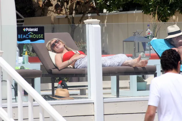 Lindsay Lohan reclining on a sun lounger in a red top and light trousers.