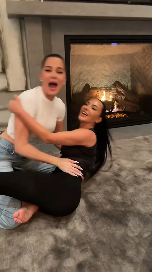 Kim Kardashian sitting beside a companion near a fireplace.
