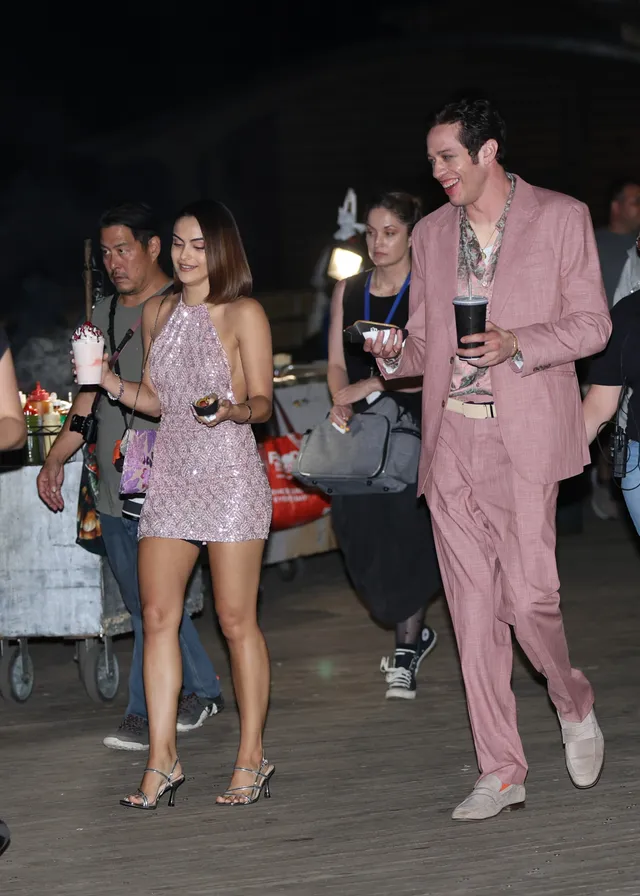 Camila Mendes walking with a group in a pink dress and metallic heels.