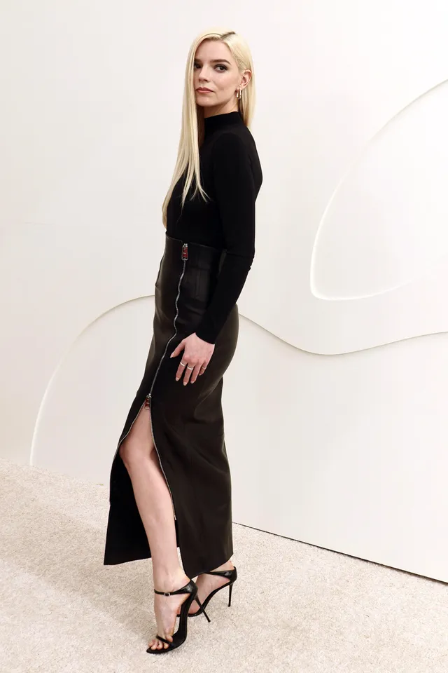 Anya Taylor-Joy posing in a long black dress and black strappy heels.