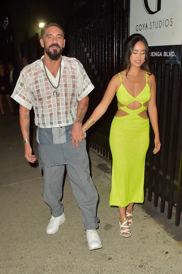 Emily Tosta walking beside a guest in a yellow dress and heels.