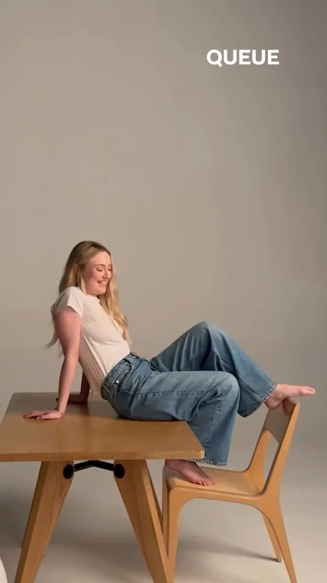 Dakota Fanning sitting barefoot in jeans and a white shirt on a table.
