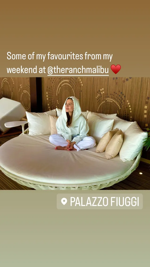 Hayley Atwell sitting cross legged on a daybed in a robe.