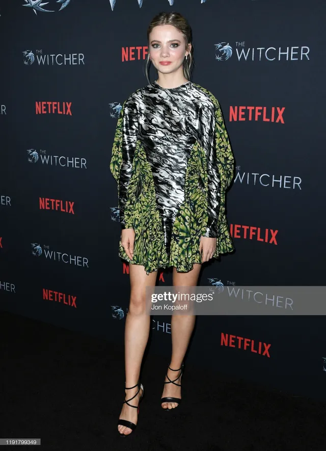 Freya Allan standing in a patterned dress and black heeled sandals.