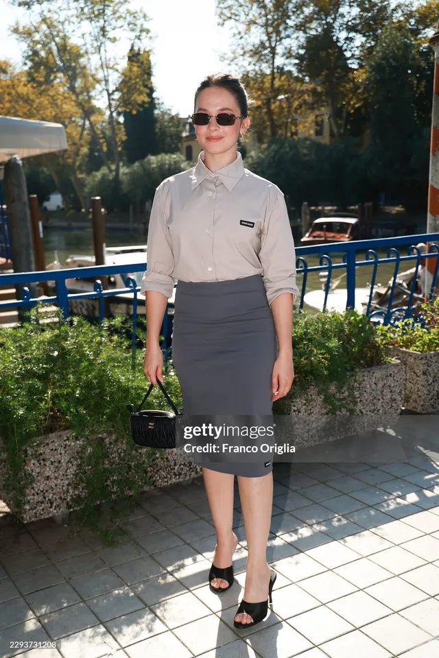 Cailee Spaeny posing outdoors in a grey skirt and black heels.