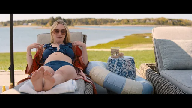 Dakota Fanning reclining barefoot on an outdoor chair by the water.