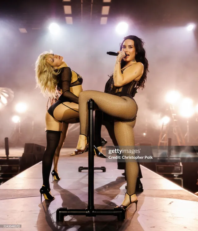 Demi Lovato sitting on stage in black platform heels.