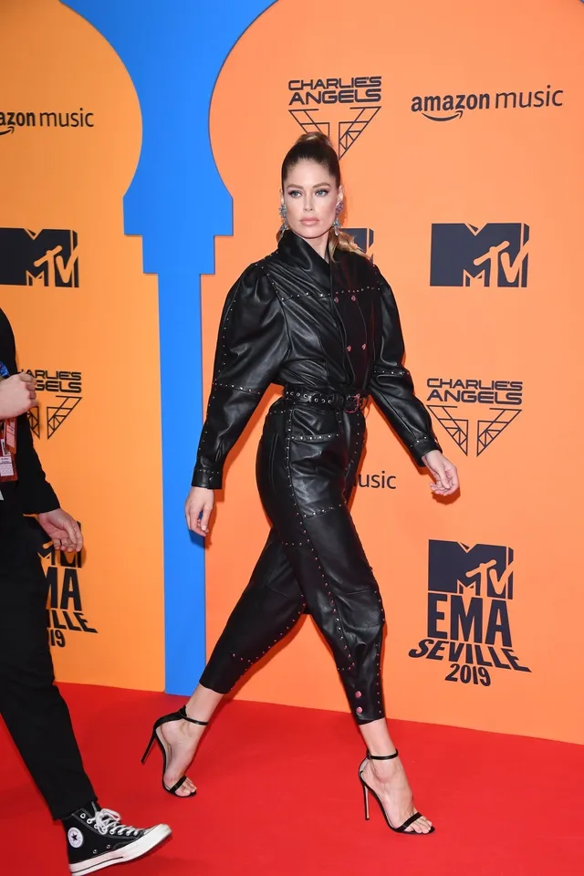 Doutzen Kroes walking in black heels and a belted black outfit on a red carpet.