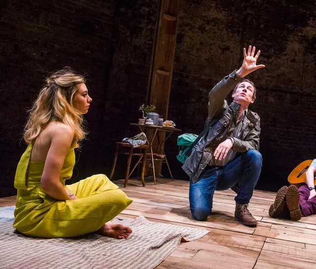 Vanessa Kirby seated on a theatre stage in a yellow outfit.