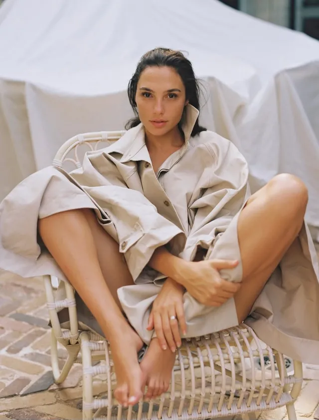 Gal Gadot sitting barefoot in a woven chair.