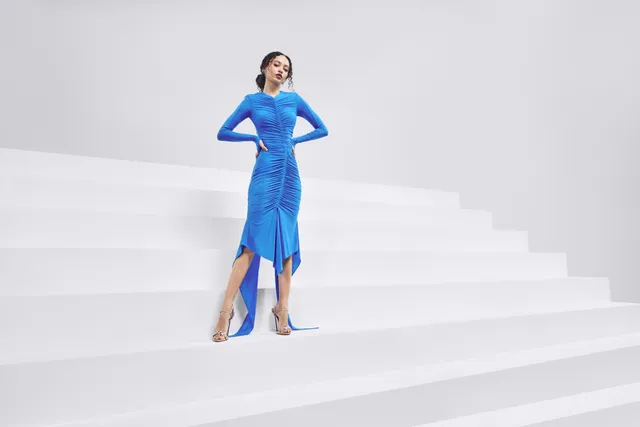 Nico Parker posing on studio steps in a blue dress and metallic heels.
