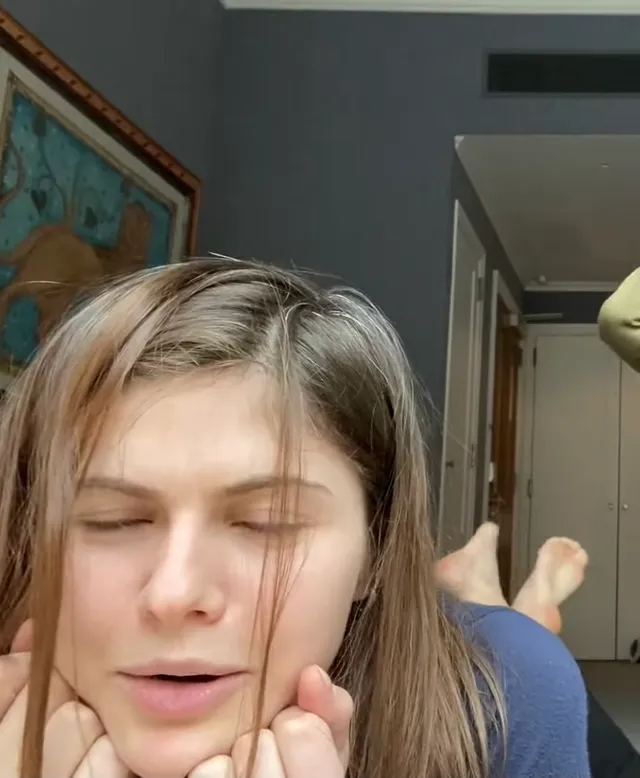 Alexandra Daddario lying indoors with bare feet raised behind her.