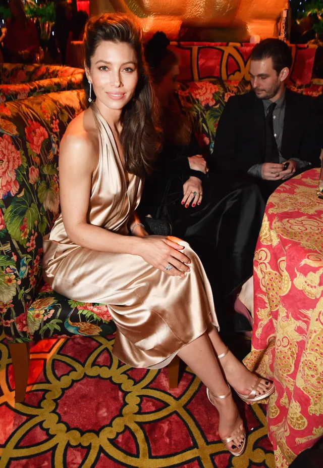Jessica Biel seated at an event in a metallic dress and heels.