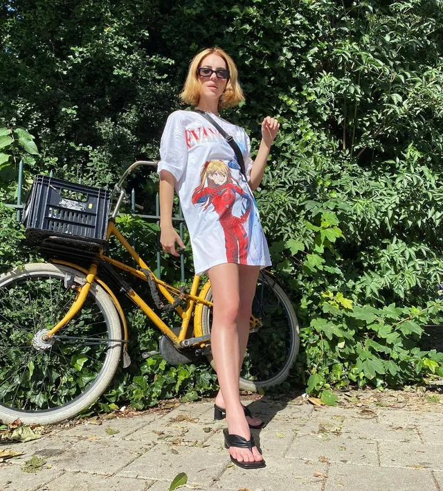 Adelaide Kane standing beside a bicycle in a T-shirt and flip-flops.