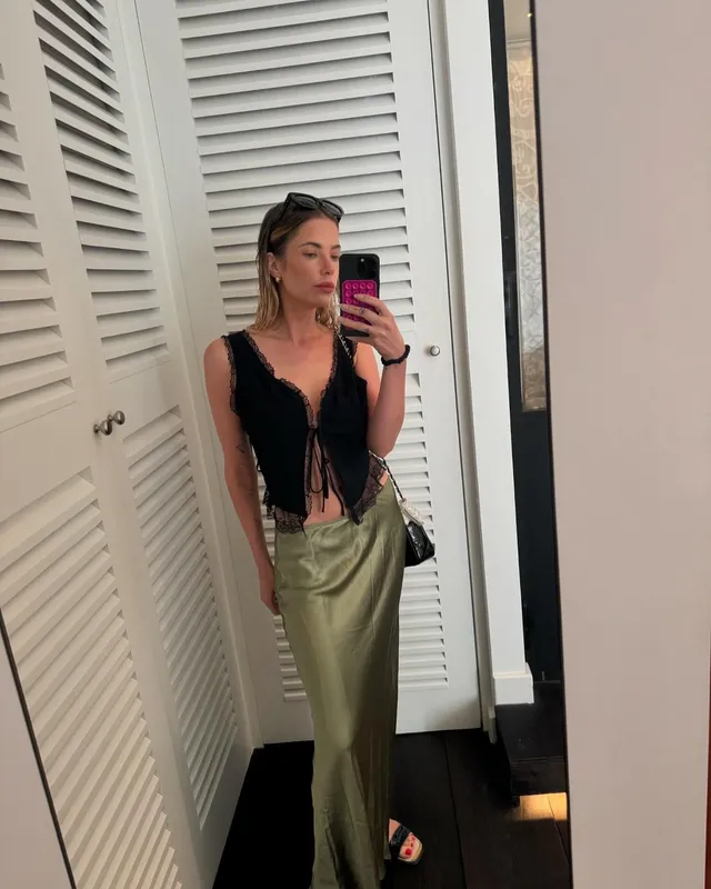 Ashley Benson taking a mirror portrait in a black top and green trousers.