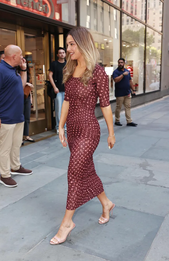 Madelyn Cline walking along a pavement in a patterned dress and pale heels.