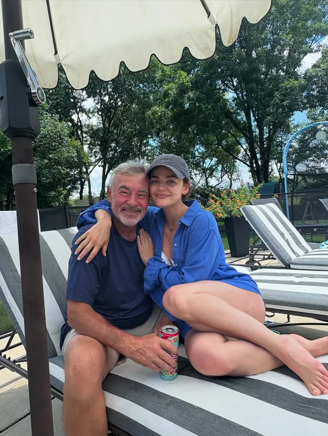 Lucy Hale sitting with a companion on a poolside lounger.