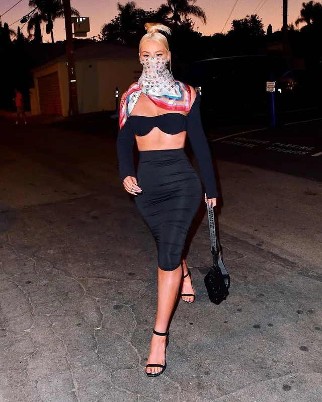 Iggy Azalea walking outdoors in a black outfit and black heels.