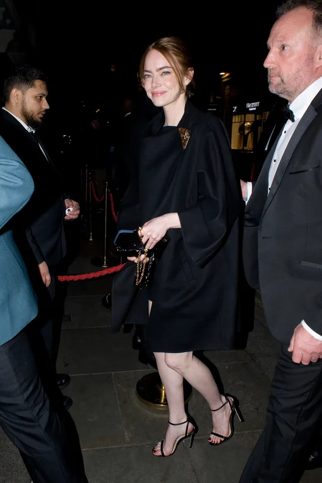 Emma Stone walking past guests in a black dress and heels.