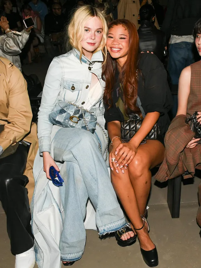 Elle Fanning sitting beside another woman in a pale outfit and sandals.