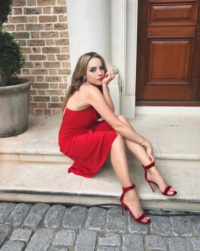 Elizabeth Gillies sitting on outdoor steps in a red dress.
