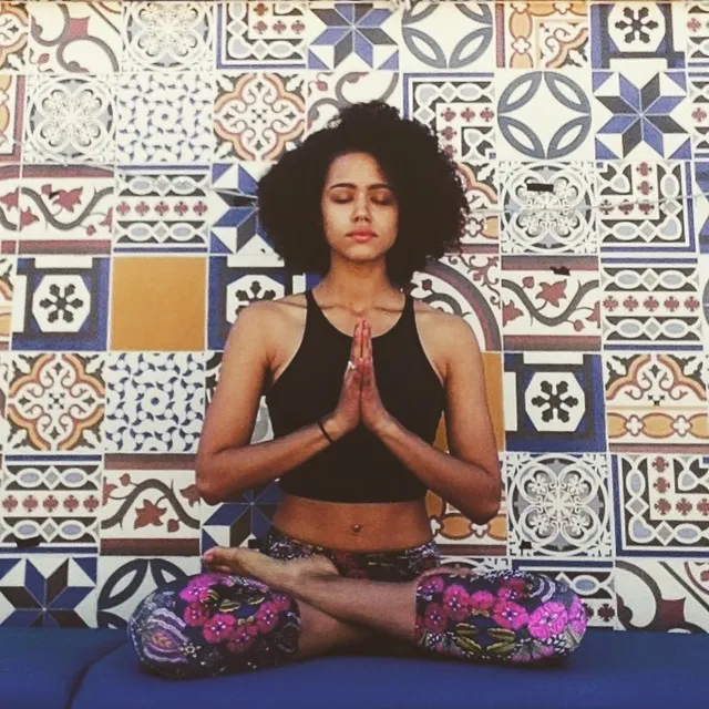 Nathalie Emmanuel sitting cross legged beside a patterned wall.