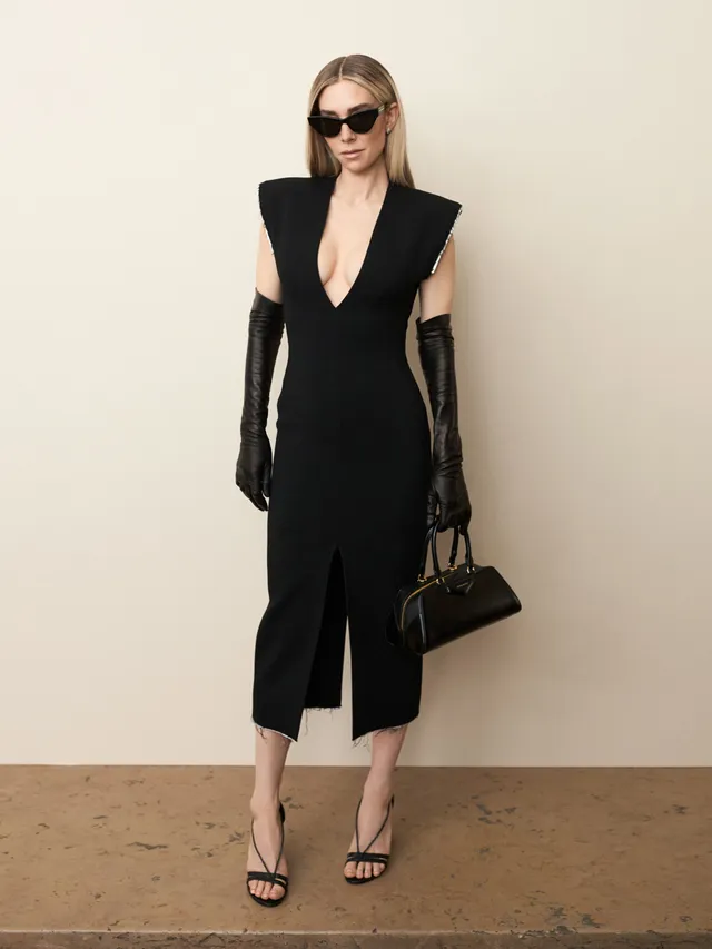 Vanessa Kirby standing in a black dress and heeled sandals for a portrait.