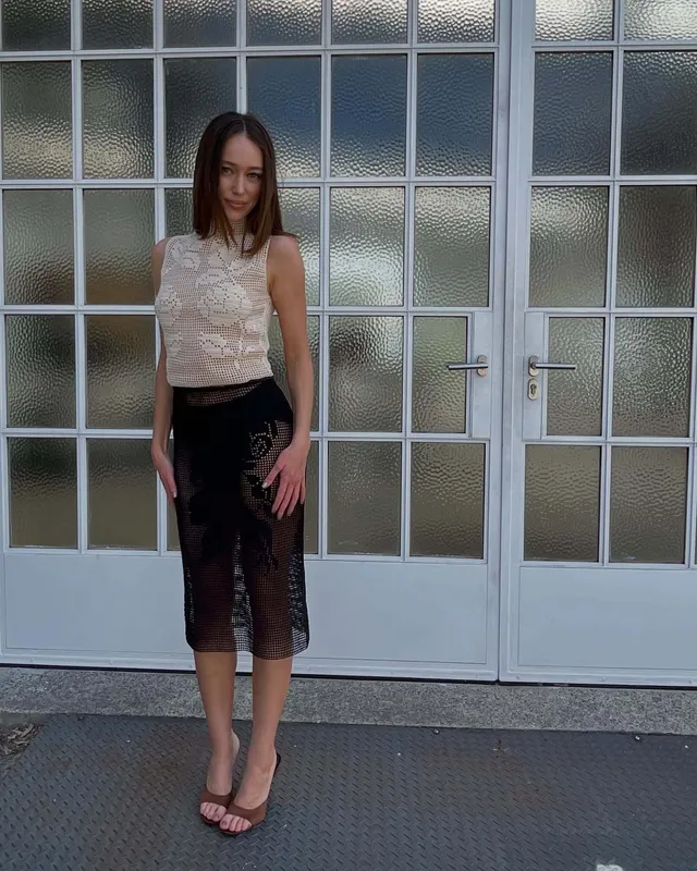 Alycia Debnam-Carey standing outside a doorway in a pale top and dark skirt.