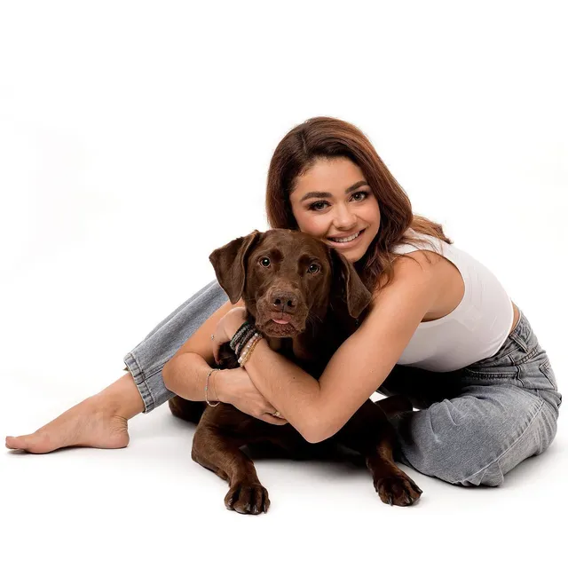 Sarah Hyland sitting with a dog during a studio portrait.