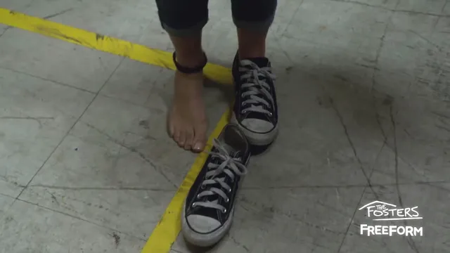 Maia Mitchell standing with one bare foot and one sneaker in a scene.